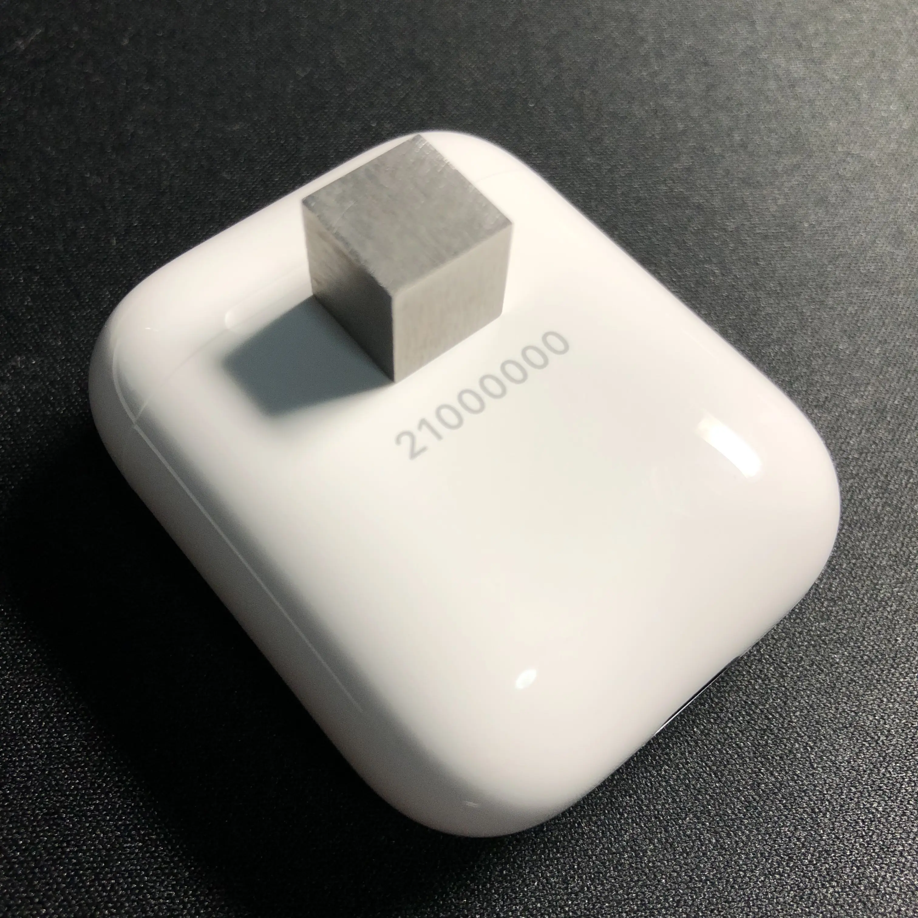 放置于AirPods充电盒上方的1cm*1cm*1cm钨块;AirPods的激光镌刻信息为“21000000”